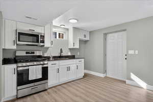 Kitchen featuring stainless steel appliances, white cabinetry, light wood finished floors, a textured ceiling, and dark stone countertops