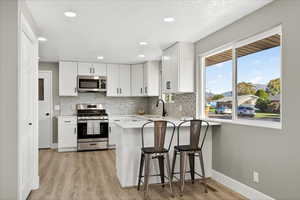Kitchen featuring stainless steel appliances, white cabinetry, backsplash, light wood-style flooring, and recessed lighting