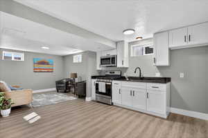 Kitchen featuring appliances with stainless steel finishes, white cabinetry, a textured ceiling, light wood finished floors, and dark stone countertops