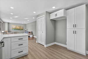 Kitchen with white cabinets, open floor plan, light wood-style floors, recessed lighting, and light stone counters