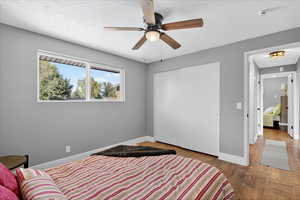 Bedroom with a textured ceiling, a closet, ceiling fan, and wood finished floors