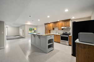 Kitchen featuring brown cabinetry, appliances with stainless steel finishes, a breakfast bar area, a kitchen island, and open shelves