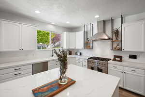 Kitchen featuring white cabinets, recessed lighting, wall chimney exhaust hood, stainless steel appliances, and a textured ceiling