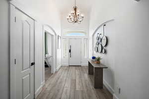 Foyer entrance featuring high vaulted ceiling, light wood-style floors, and a chandelier