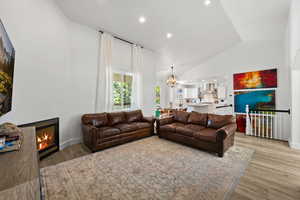 Living room with a chandelier, recessed lighting, a glass covered fireplace, light wood finished floors, and high vaulted ceiling