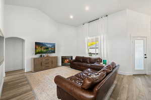 Living room featuring a glass covered fireplace, light wood-style flooring, recessed lighting, high vaulted ceiling, and arched walkways