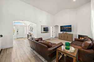 Living room featuring high vaulted ceiling, arched walkways, light wood-type flooring, and a lit fireplace