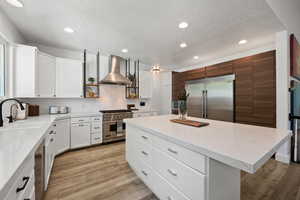 Kitchen with a center island, white cabinetry, a textured ceiling, recessed lighting, and wall chimney exhaust hood