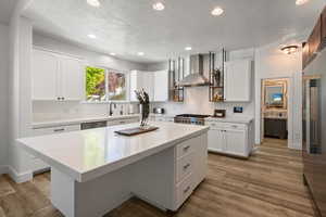 Kitchen with recessed lighting, wall chimney range hood, white cabinets, light wood finished floors, and appliances with stainless steel finishes