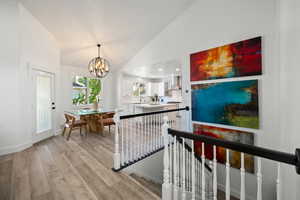 Corridor with an upstairs landing, light wood-style floors, a chandelier, and high vaulted ceiling