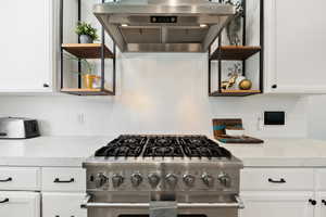 Kitchen featuring open shelves, under cabinet range hood, stainless steel stove, and white cabinetry