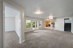 Unfurnished living room featuring light carpet, a textured ceiling, and stairway