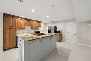 Kitchen featuring light stone counters, brown cabinetry, recessed lighting, a center island, and appliances with stainless steel finishes