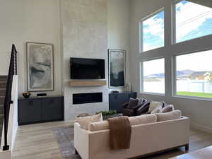 Living area featuring stairs, healthy amount of natural light, a tiled fireplace, light wood-style flooring, and a high ceiling