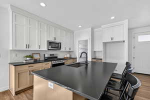 Kitchen with an island with sink, appliances with stainless steel finishes, dark wood-style flooring, a breakfast bar, and tasteful backsplash
