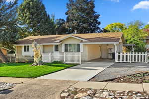 Ranch-style home with a fenced front yard, a shingled roof, concrete driveway, and a carport