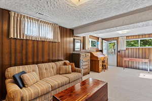 Living area with light colored carpet, wooden walls, and a textured ceiling