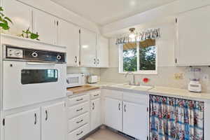 Kitchen with white appliances, light countertops, backsplash, and white cabinetry