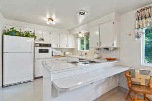 Kitchen featuring light countertops, white appliances, tasteful backsplash, and a peninsula