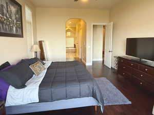 Bedroom with arched walkways, dark wood-style floors, connected bathroom, and recessed lighting