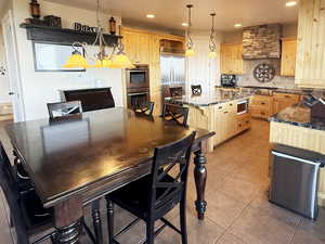 Kitchen with light tile patterned flooring, pendant lighting, backsplash, appliances with stainless steel finishes, and a center island