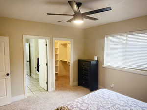 Bedroom featuring light carpet, a spacious closet, a ceiling fan, and light tile patterned floors