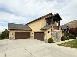 View of side of home with a balcony, stone siding, stucco siding, and concrete driveway