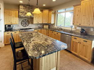 Kitchen with backsplash, a breakfast bar area, a center island, stainless steel appliances, and light tile patterned floors
