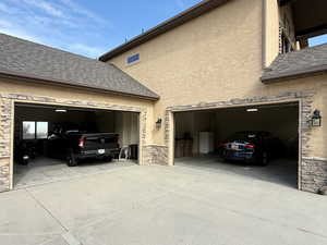 View of home's exterior with concrete driveway, stone siding, a shingled roof, and stucco siding