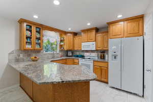 Kitchen featuring a huge peninsula, white appliances, granite countertops, decorative backsplash, large pantry, and light marble finish flooring