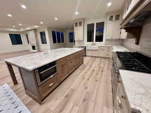 Kitchen with two tone cabinetry, light stone countertops, light wood-style floors, open floor plan, and stainless steel appliances