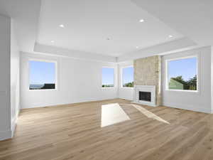 Lliving room with a raised ceiling, a fireplace, light wood finished floors, healthy amount of natural light, and recessed lighting