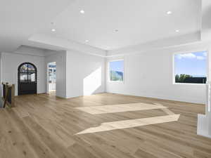 Room with healthy amount of natural light, a raised ceiling, light wood-style floors, and recessed lighting