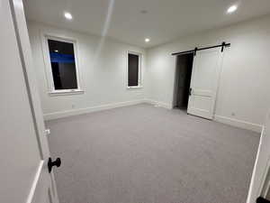 Unfurnished bedroom featuring a barn door, carpet, and recessed lighting