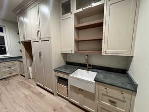 Kitchen featuring open shelves, light wood-style flooring, dark stone counters, and glass fronted cabinets