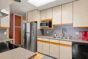 Kitchen featuring black appliances, tasteful backsplash, exhaust hood, and cream cabinets