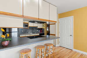 Kitchen featuring a kitchen bar, white cabinets, light wood-type flooring, dark countertops, and stainless steel appliances
