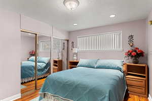 Bedroom featuring wood finished floors, recessed lighting, a textured ceiling, and multiple closets