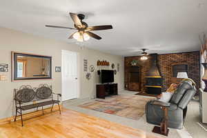 Living room featuring wood finished floors, a wood stove, brick wall, a textured ceiling, and ceiling fan
