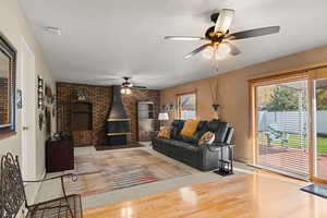 Living room featuring wood finished floors, a textured ceiling, a wood stove, brick wall, and a ceiling fan