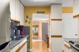 Kitchen featuring appliances with stainless steel finishes, white cabinets, dark countertops, light wood finished floors, and tasteful backsplash