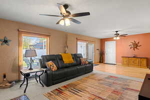 Living area with a textured ceiling, a textured wall, ceiling fan, and light carpet