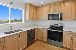 Kitchen with light brown cabinets, appliances with stainless steel finishes, light wood-style flooring, recessed lighting, and light stone counters