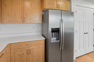 Kitchen with stainless steel fridge, light brown cabinets, light wood-style flooring, and light stone countertops