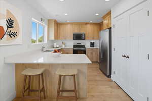 Kitchen with a peninsula, stainless steel appliances, a kitchen bar, light wood-style flooring, and light wood finish cabinetry