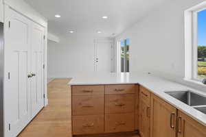 Kitchen featuring recessed lighting, a peninsula, light wood-style floors, light stone counters, and brown cabinets