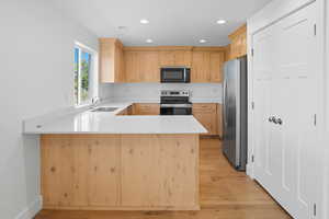 Kitchen with light brown cabinets, a peninsula, appliances with stainless steel finishes, light wood finished floors, and recessed lighting