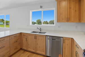 Kitchen with dishwasher, light stone counters, light brown cabinetry, and light wood-style flooring