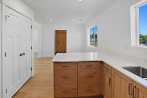 Kitchen with recessed lighting, light wood finished floors, a peninsula, light stone counters, and brown cabinetry