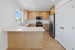 Kitchen with a peninsula, light brown cabinetry, appliances with stainless steel finishes, recessed lighting, and light wood-style flooring